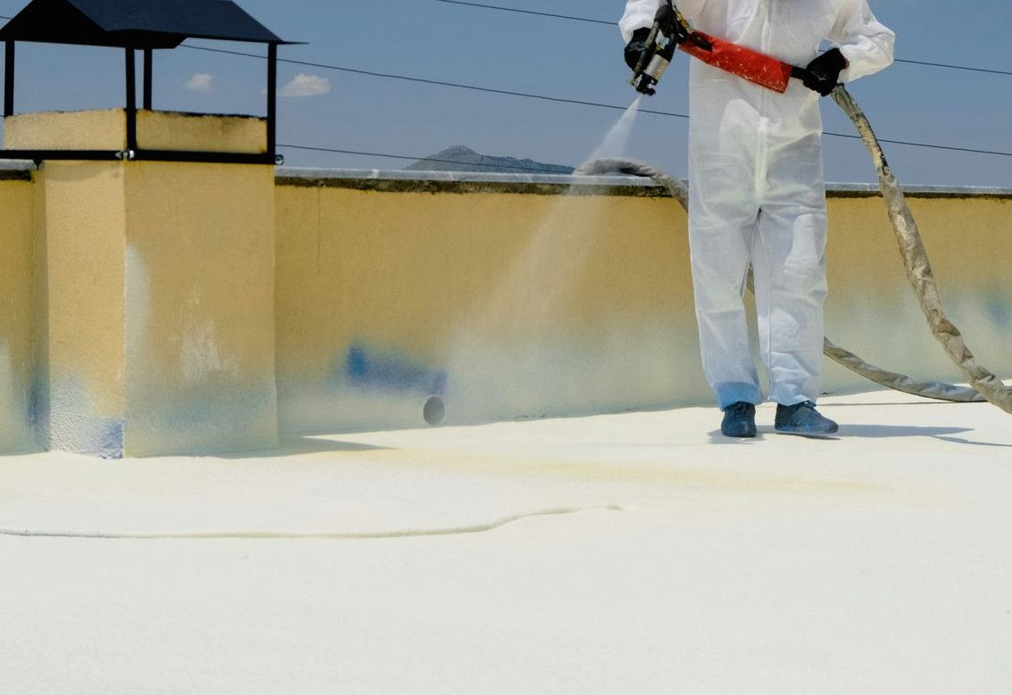 a man in a white coverall spray painting a roof